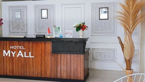 A hotel reception area with a wooden reception desk, framed pictures on the wall, and a green patterned rug on the floor. - Hotel My All Padang (Padang)