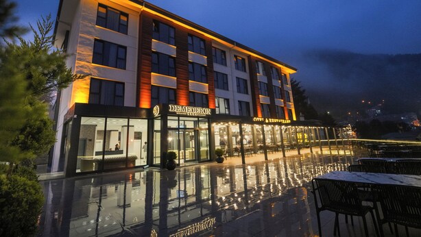 Een modern hotel met een glazen gevel, terras en een reflecterend zwembad.