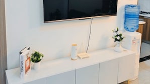 A modern living room with a flat-screen TV mounted on the wall, a white console table with decorative items, and a water dispenser. - Valley Heights Apartments (Nairobi)