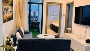 A modern hotel room with a sofa, a round table, a bed, a TV, and a view of the city. - Valley Heights Apartments (Nairobi)
