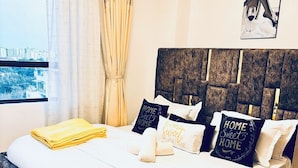A neatly made bed with pillows, a view of the city through a window, and a cityscape visible outside. - Valley Heights Apartments (Nairobi)