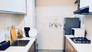 A compact kitchen with white cabinets, a black refrigerator, a stove, and a microwave. There are two wooden cutting boards on the floor. - Valley Heights Apartments (Nairobi)