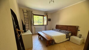 Un dormitorio con cama de madera, un banco, una mesita de noche, un radiador y una ventana con cortinas.