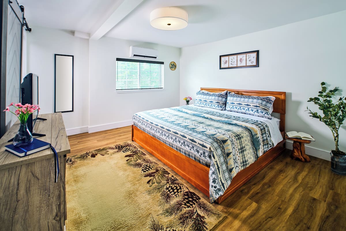 Un dormitorio con una cama de madera, un ventanal con persianas, una lámpara de pie y una planta en maceta.