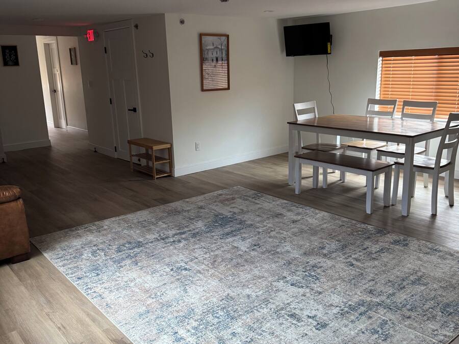 Un vaste espace de vie comprenant une table à manger, des chaises, une grande moquette et un téléviseur à écran plat fixé au mur.