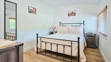 Un dormitorio con una cama, un aparador, una mesita de noche, un espejo y dos cuadros colgados en la pared.