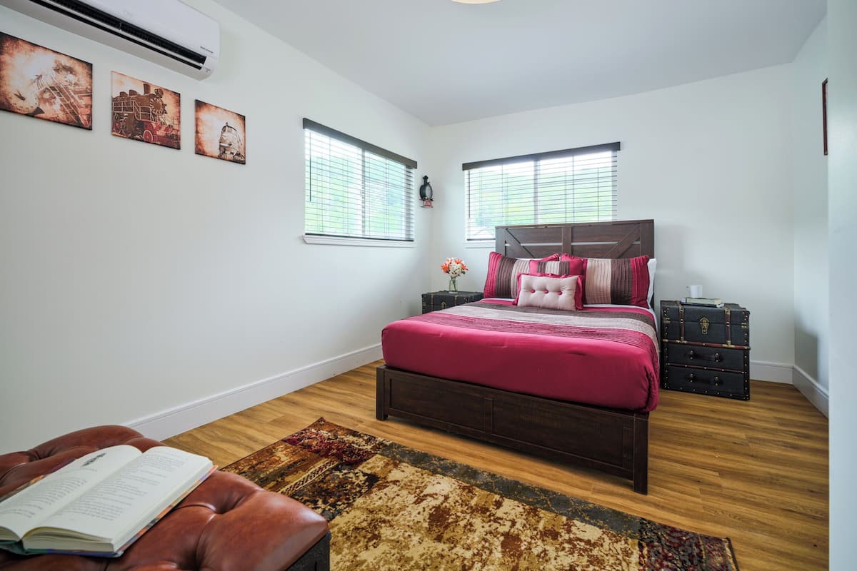 Un dormitorio con una cama grande, dos ventanas con persianas, piso de madera y una alfombra.