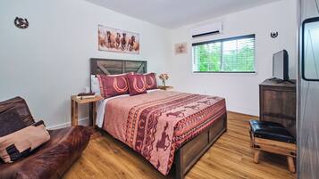 A bedroom with a wooden bed, a leather couch, a wooden nightstand, a TV, and a window with blinds.