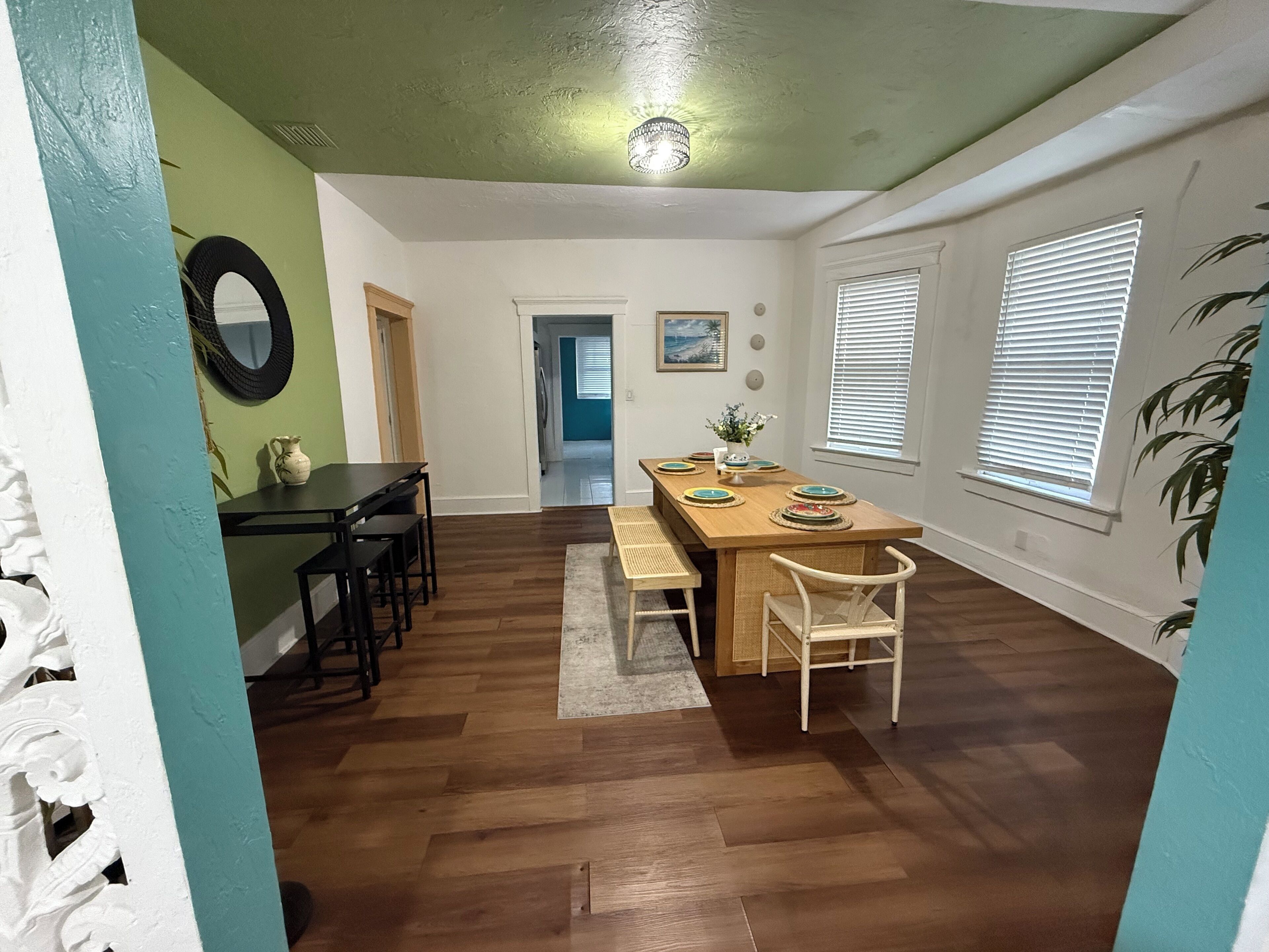 A dining area with a wooden table and chairs, a small rug, and a ceiling light fixture.
