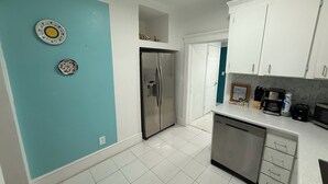 Une cuisine avec des armoires blanches, un réfrigérateur en acier inoxydable et un lave-vaisselle. Deux assiettes décoratives sont accrochées au mur.