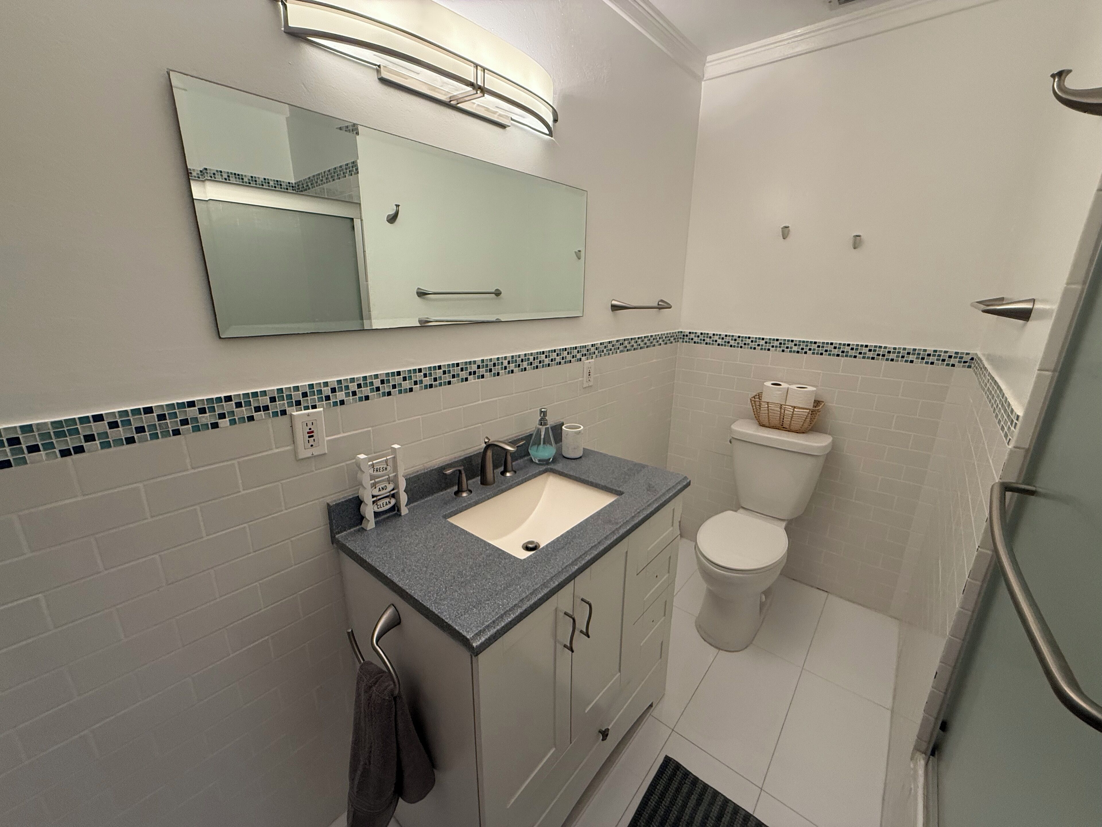 A bathroom with a sink, mirror, toilet, and shower area.
