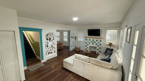 Un salon spacieux avec un canapé blanc, un parquet en bois, une cheminée et un escalier.