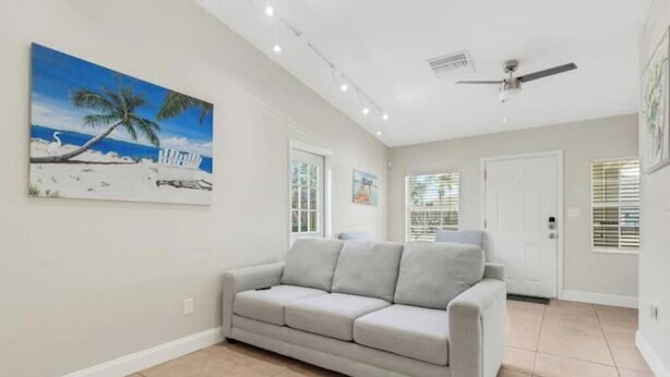A living room with a beige sofa, a ceiling fan, and a painting of a beach scene.