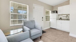 A compact living space with a kitchenette, a grey armchair, and a glass table.