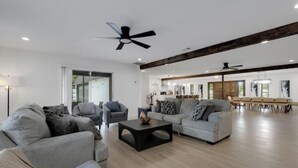 A spacious living room with a modern design, featuring a large sofa, a coffee table, and a dining area with a long table and chairs. - Sarasota Paradise Special Events (Sarasota)