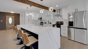 A modern kitchen with white cabinetry, stainless steel appliances, and a large island with bar stools. - Sarasota Paradise Special Events (Sarasota)