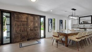 A spacious dining area with a large wooden table and modern chairs, a large mirror above the table, and a sliding glass door leading to an outdoor area. - Sarasota Paradise Special Events (Sarasota)
