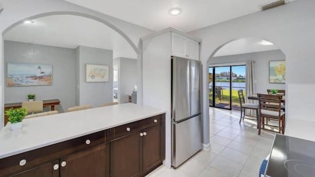 A modern kitchen with a stainless steel refrigerator, white cabinetry, and a large island. - Sunseeker Paradise for 8! (Port Charlotte)