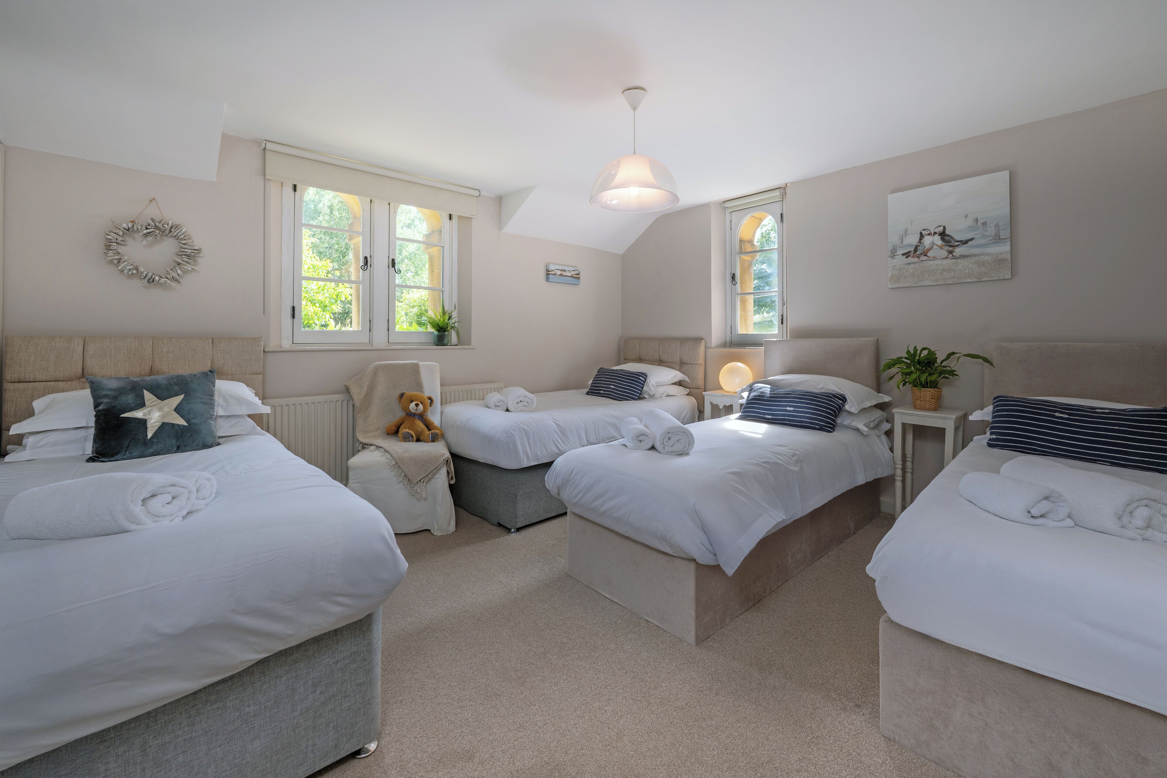 A hotel room with three beds, a large window, a ceiling light, and a wall decoration.