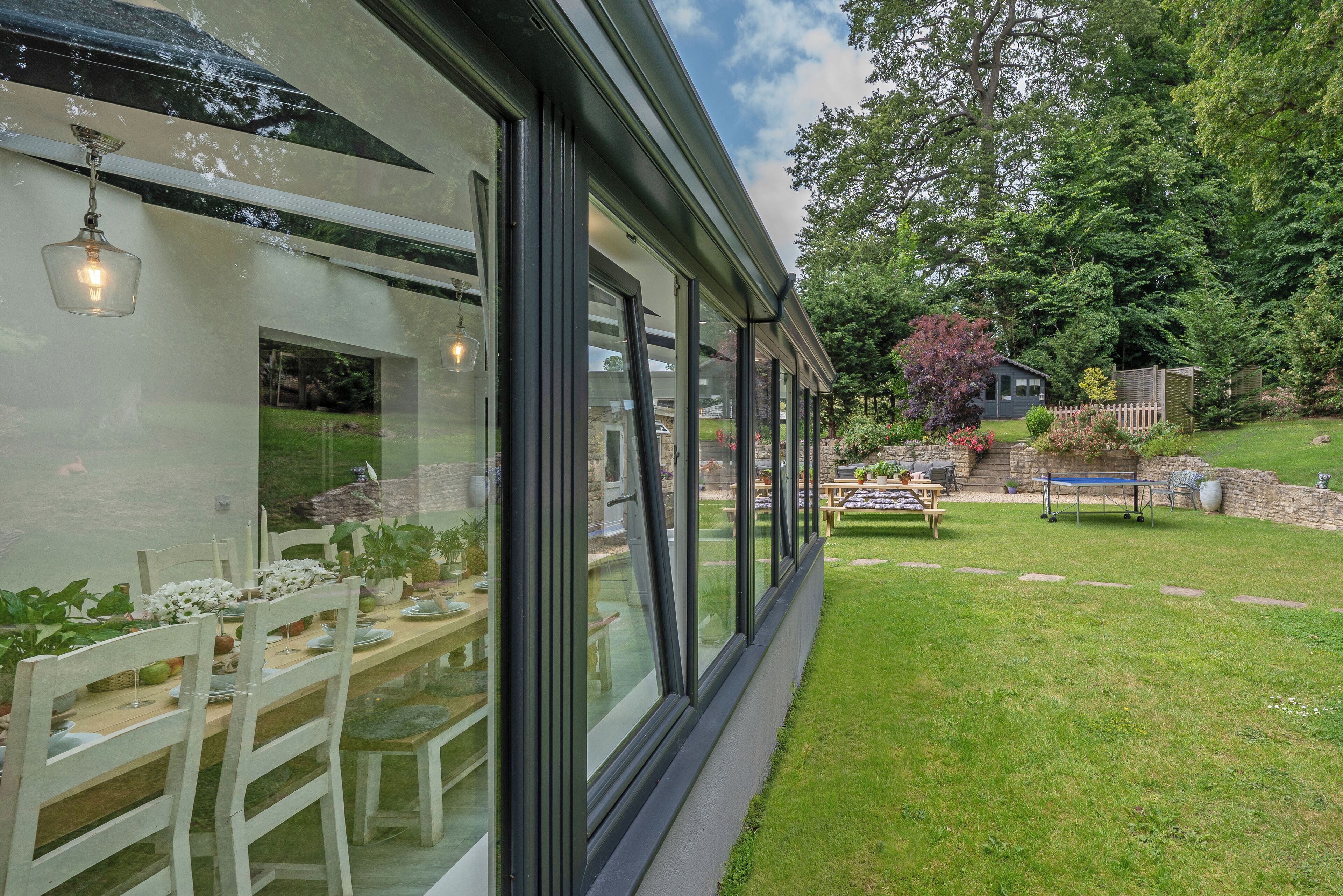 Ein modernes Haus mit großen Fenstern, einem Essbereich mit Tisch für vier Personen und einem gepflegten Garten.