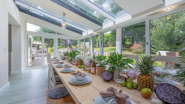 Un espace de restauration moderne, avec une longue table dressée pour le repas, de grandes fenêtres et une vue sur le jardin.