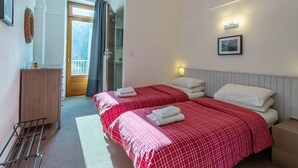 Habitación de hotel con dos camas, un armario de madera, una mesita y una ventana con cortinas.