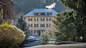 Un edificio de dos pisos con techo inclinado, rodeado de árboles cubiertos de nieve y una montaña al fondo.