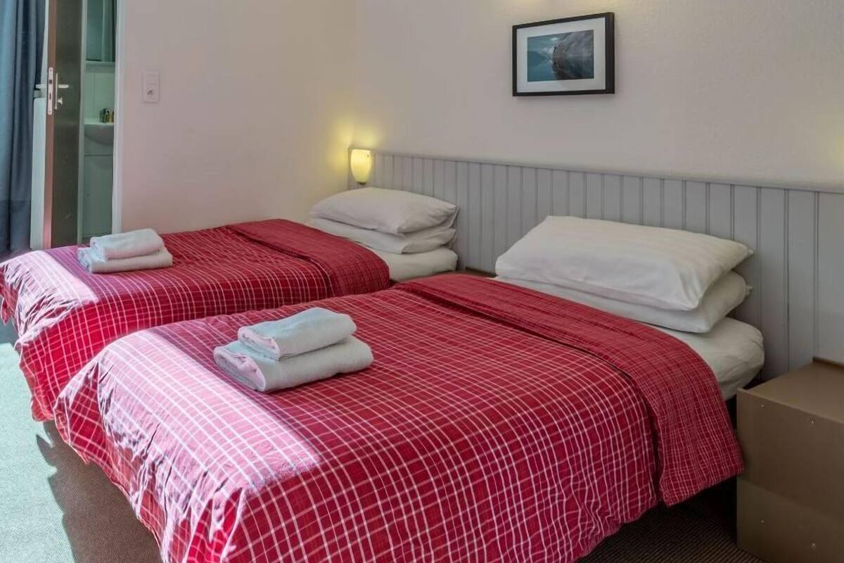 A hotel room with two beds, each with red and white bedding, a framed picture on the wall, and a nightstand with a box.