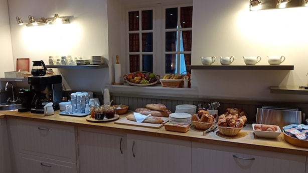 Una cocina con barra de desayuno, que incluye cafeteras, cestas de fruta, pasteles y otros productos para el desayuno.