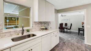 A modern kitchen with white cabinets, a large window, and a dining area with a table and chairs. - Tropical Paradise for 8 (Bradenton)