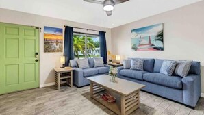 A living room with a green door, a ceiling fan, a blue sofa, a coffee table, and artwork on the walls. - Tropical Paradise for 8 (Bradenton)
