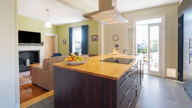 A modern kitchen with a central island, a built-in oven, and a dining area with a sofa. - Rose Cottage Charming Haven near CBD and Waterfront (North Hobart)
