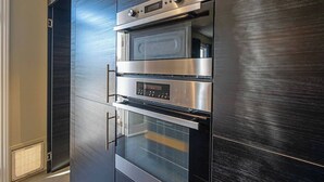 A modern kitchen with a built-in oven and microwave, stainless steel appliances, and a dark wood finish. - Rose Cottage Charming Haven near CBD and Waterfront (North Hobart)