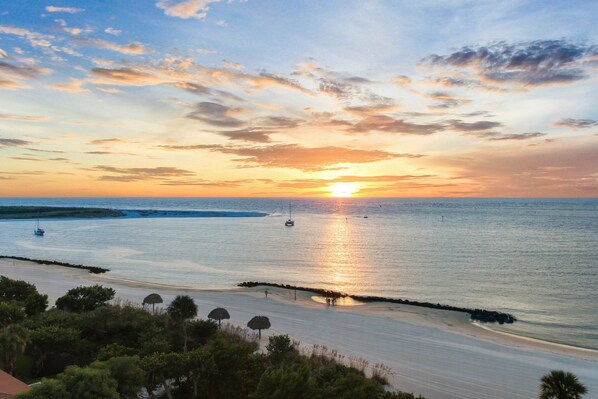 A beach with a sunset, calm sea, and a few boats.