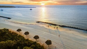 Ein Strand mit Sonnenuntergang, ruhiger See und einigen Booten.