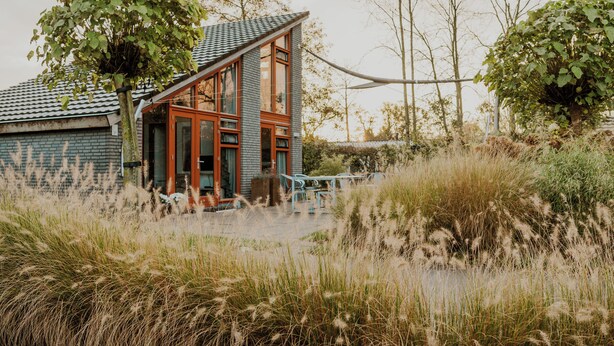 A modern house with a sloped roof, large windows, and a visible outdoor seating area. - Dutchen Vakantiepark Buiten Bergen (Schoorl)