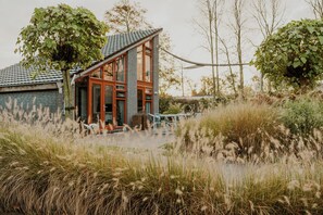 A modern house with a sloped roof, large windows, and a visible outdoor seating area. - Dutchen Vakantiepark Buiten Bergen (Schoorl)