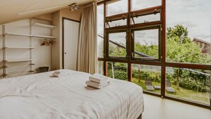 A bedroom with a large window, a bed with white linens, a wardrobe, and a shelf unit. - Dutchen Vakantiepark Buiten Bergen (Schoorl)