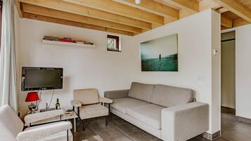 A living room with a sofa, two armchairs, a TV, a painting, and a wooden ceiling.