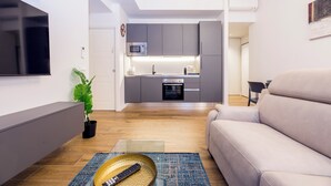 Un soggiorno moderno con divano, TV a schermo piatto, angolo pranzo con tavolo e sedie e cucina con pensili grigi e forno a microonde.