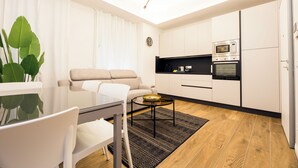 Un soggiorno moderno con un divano, un tavolo da pranzo con sedie, un tavolino da caffè, una zona cucina con forno a microonde e forno, e un'ampia finestra con tende.