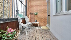 Une terrasse en bois avec deux chaises blanches et une petite table, une plante en pot et un mur de briques.
