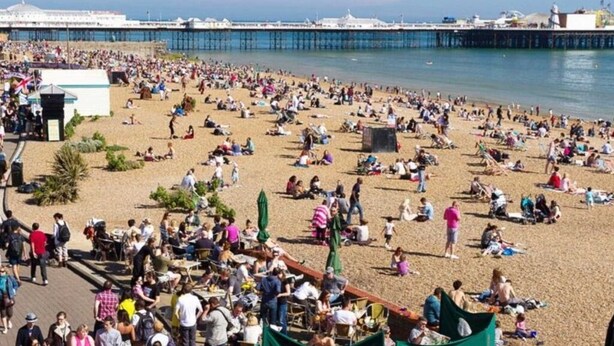 Une plage bondée où les gens se prélassent au soleil et se promènent le long du rivage.
