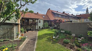 A residential area with a paved pathway leading to a house with a wooden pergola and potted plants.