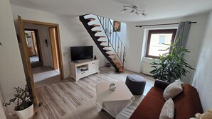 A living room with a wooden staircase, a television on a white cabinet, a potted plant, and a sofa.