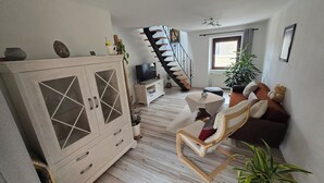 A living room with a wooden cabinet, a TV, a sofa, and a staircase.