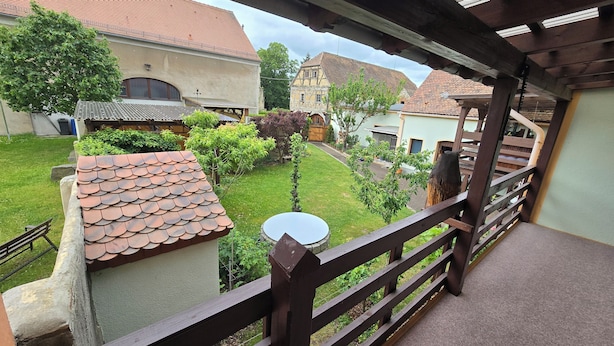 A balcony with a view of a courtyard, featuring a tiled roof, a wooden fence, and a small round table.