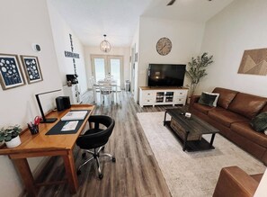 Una sala de estar moderna con una mesa de comedor de madera, un sofá de cuero marrón, un televisor y una estantería.