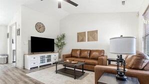 A modern living room with a flat-screen TV, leather sofa, coffee table, and a lamp.