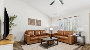 A living room with two brown leather sofas, a coffee table, a TV, and a window with blinds. - Reid Cottage |3Bd/2Bth Ranch |King Beds |Sleeps 8 (Charlotte)